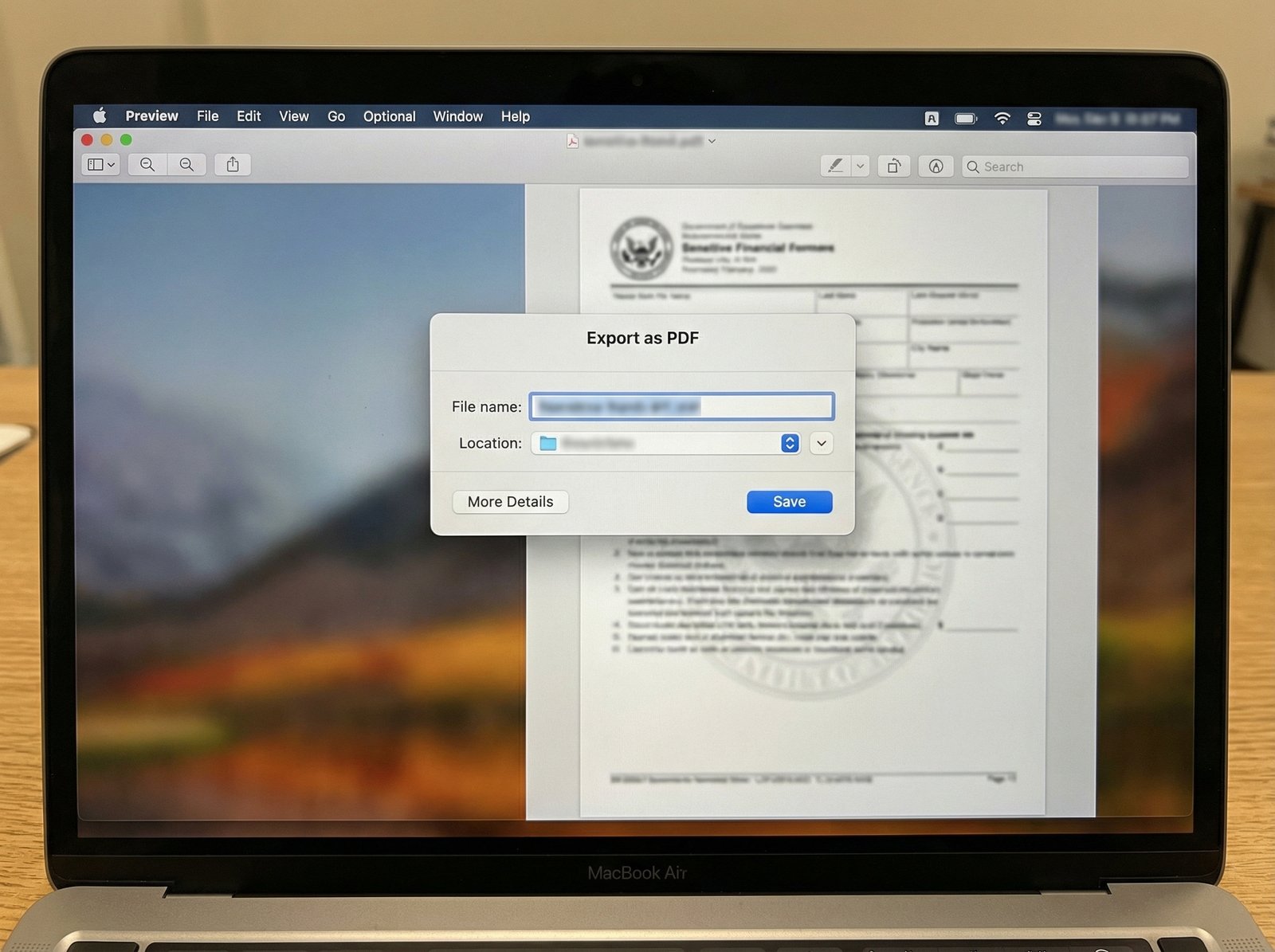 A close-up of a MacBook screen displaying the Preview app with an image open. The "Export as PDF" dialog box is active, showing options for file name, location, and a "More Details" button. A sensitive tax document is faintly visible in the background. no visible text, 4:3 aspect ratio, informational style.
