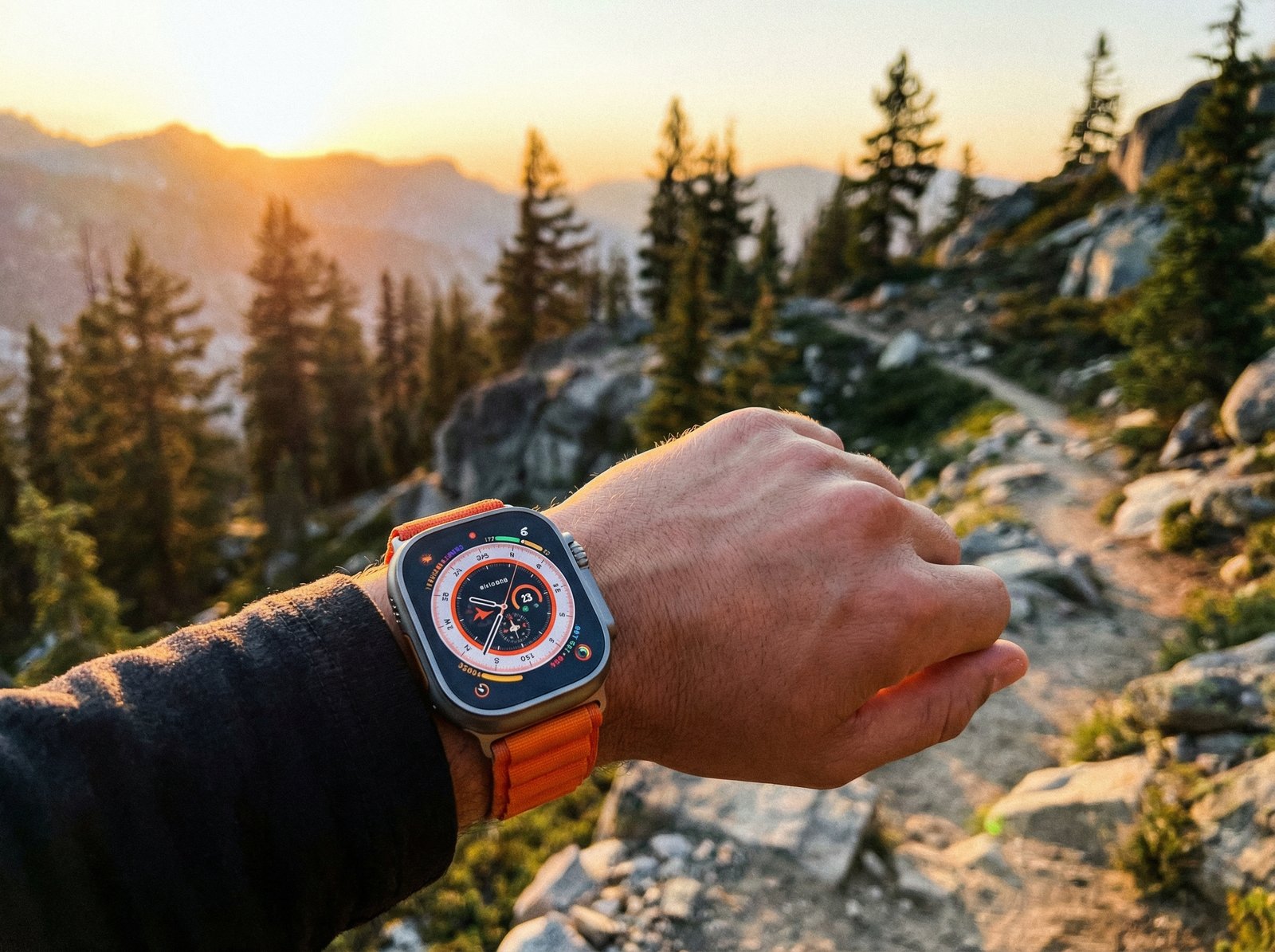 Lifestyle photography of an Apple Watch Ultra 3 worn on a wrist, in a natural outdoor setting with warm lighting. The watch face shows a detailed modular ultra face. no visible text, aspect ratio 4:3