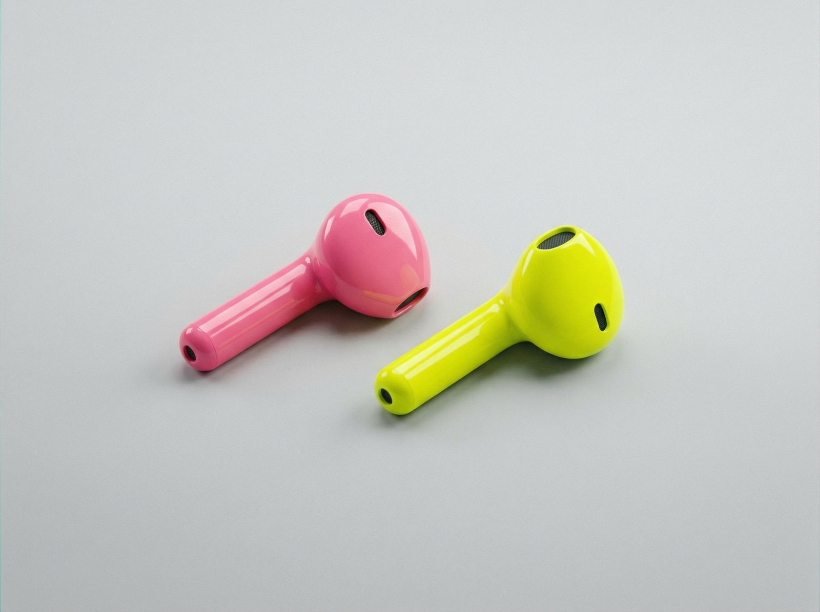 A pair of first generation wireless earbuds in vibrant candy pink and bright neon yellow colors resting on a smooth minimalist surface, high quality product photography, 4:3, no visible text
