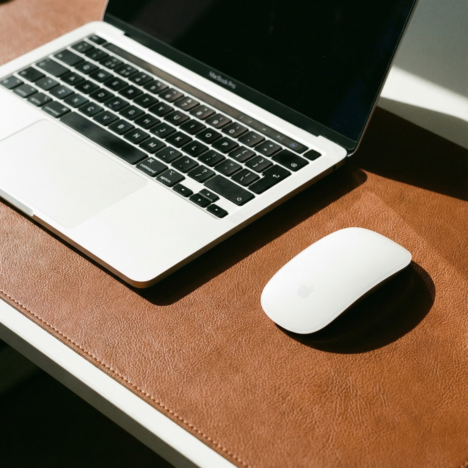 Close-up shot of a well-organized Mac workspace, featuring a minimalist eco-leather desk mat with a MacBook and a wireless mouse. Focus on clean lines and functional aesthetics. Modern layout, high contrast lighting. No visible text. 1:1 aspect ratio.