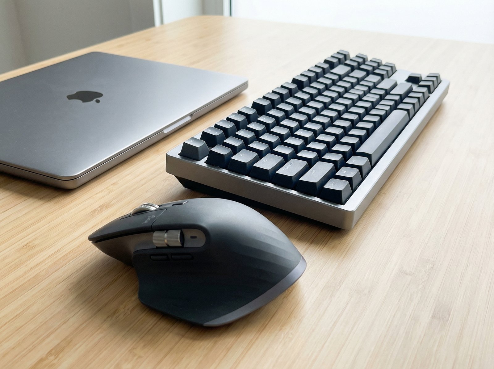 A close-up shot of an ergonomic third-party mouse, like Logitech MX Master 3S, and a mechanical keyboard, like Keychron, on a clean desk. The items are neatly arranged next to a Mac. The lighting is bright and even. aspect ratio 4:3, no visible text, no Korean text