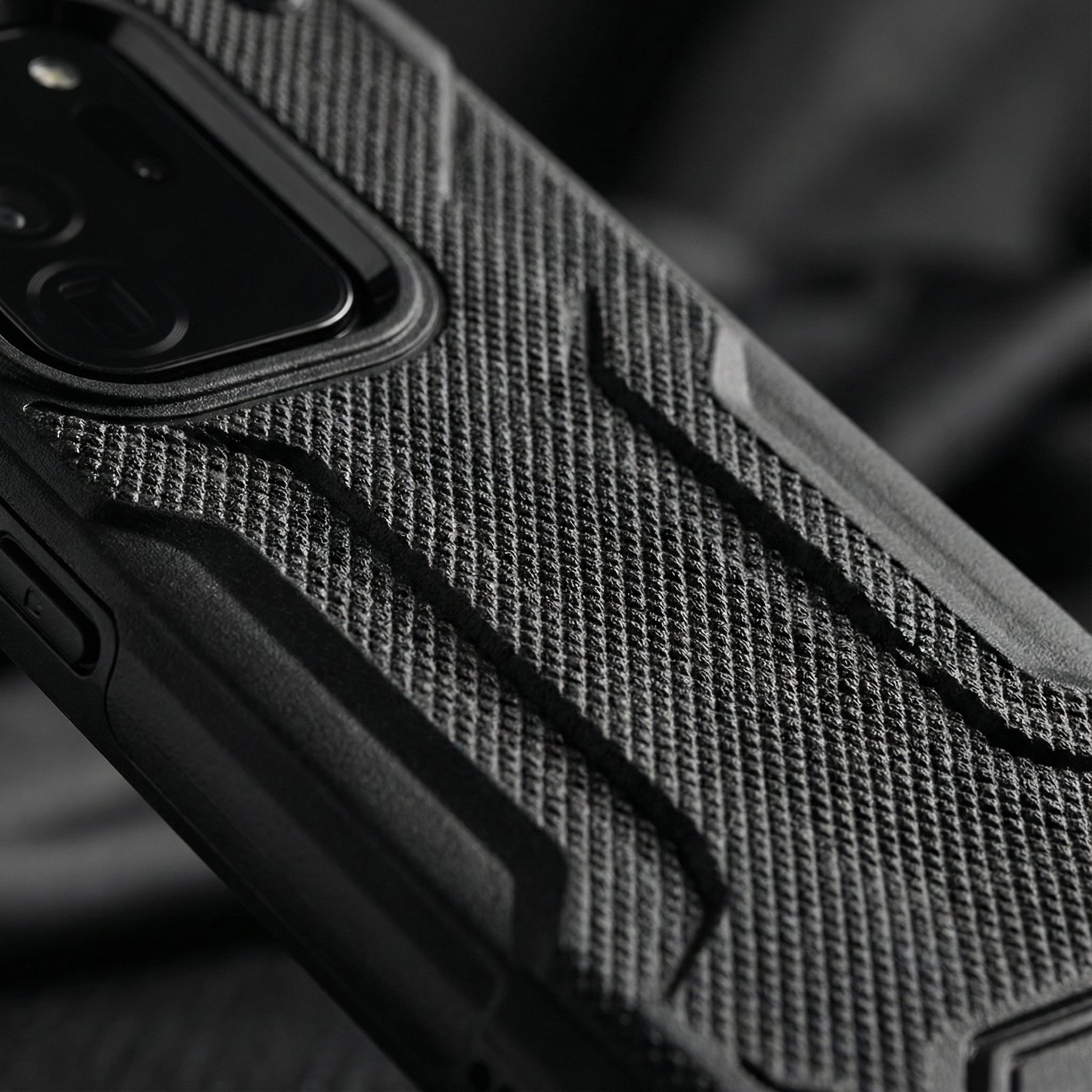 Close-up of a textured grip on a black smartphone case, showing detailed rugged surface, professional studio lighting, high contrast, 1:1, no text