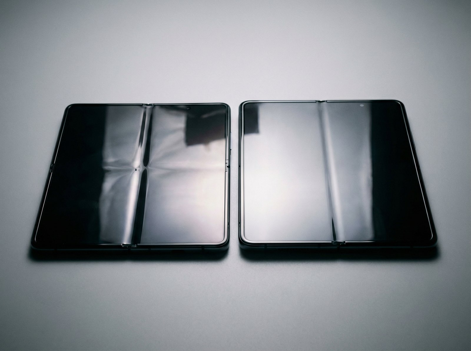 Comparison of two foldable screens side by side, one with a visible crease and one with a perfectly smooth mirror-like surface, professional studio lighting, 4:3 aspect ratio, no visible text