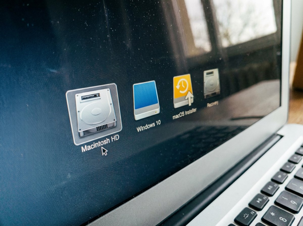 A macro shot of a laptop screen showing the macOS boot picker menu with multiple drive icons, one being a yellow installer disk. High detail, realistic composition. 4:3